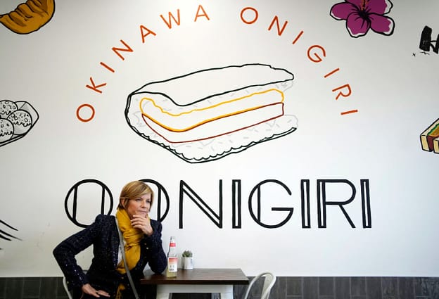 Person stands in front of a sign that says "Okinawa Onigiri" at a restaurant