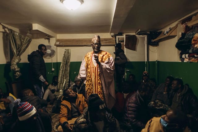 An African man stands and speaks to a crowd in a cramped space