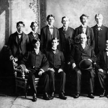 Old Black and White image, men dressed in suits are standing behind men dressed in suits who are sitting