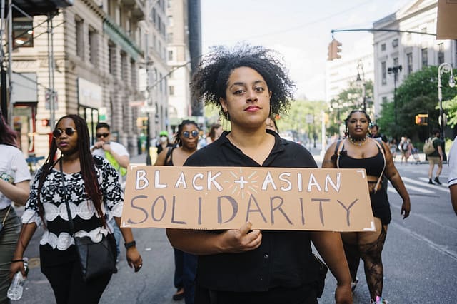 During a march, a person holds up a sign that says "Black Asian Solidarity"