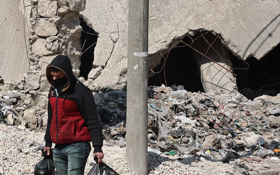A person wearing a jacket and mask surrounded by rubble